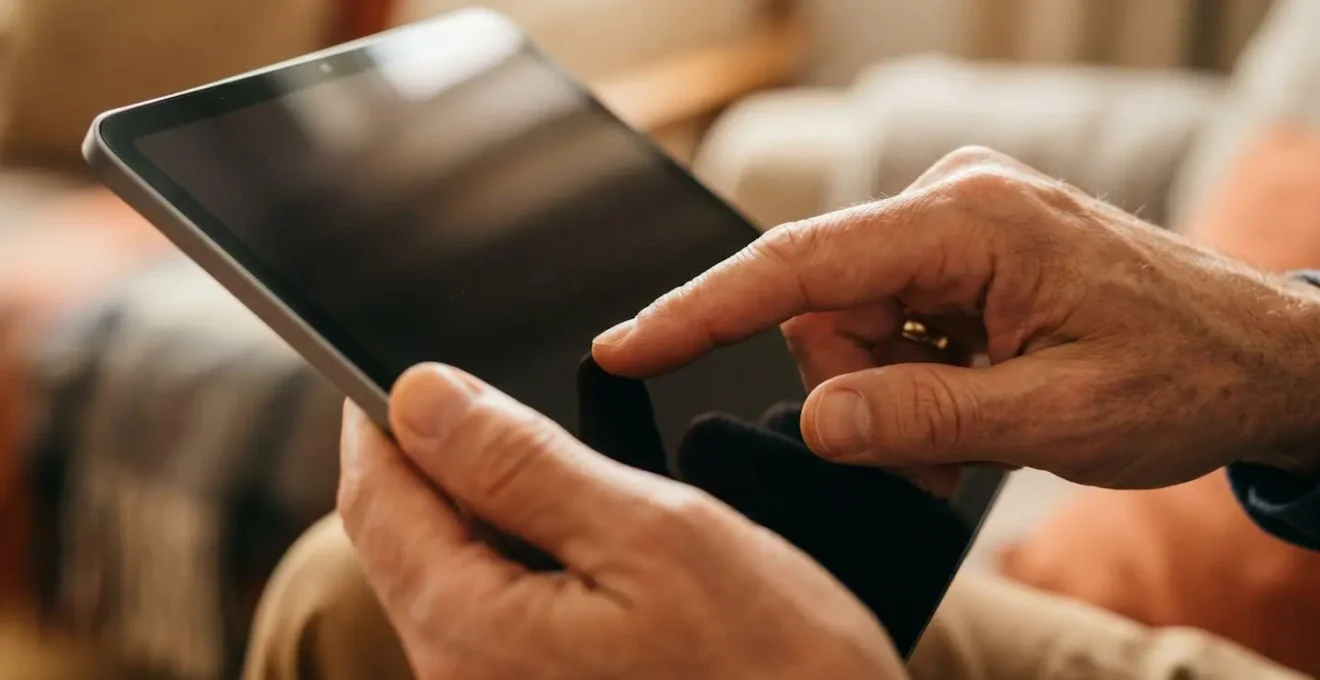 Close-up of a patient's hands interacting with a digital health portal on a tablet in a comfortable home setting.