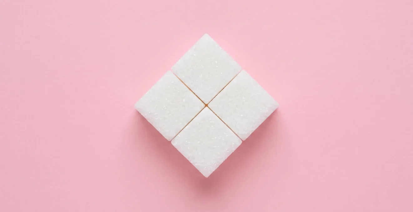 Two white sugar cubes touching at their corners against pastel pink background, viewed from directly above in symmetrical composition